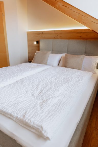 Doppelbett mit weißen Bettdecken und Kissen in einem hellen, modernen Raum.