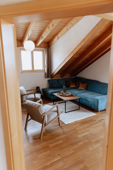 Gemütliches Wohnzimmer mit blauem Sofa, Sessel und Holzboden unter schrägen Decken.