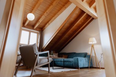 Gemütliches Zimmer mit schrägen Decken, einem blauen Sofa und einer Stehlampe.