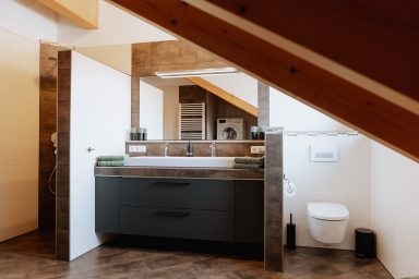 Moderne Badezimmerausstattung mit Holzakzenten und viel Stauraum unter einer Dachschräge.