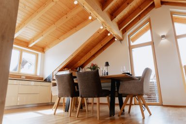 Heller, moderner Essbereich mit Holztisch und Stühlen unter einer schrägen Holzdecke.