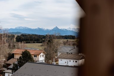 Blick auf eine ländliche Gegend mit Bergen im Hintergrund und Häusern im Vordergrund.