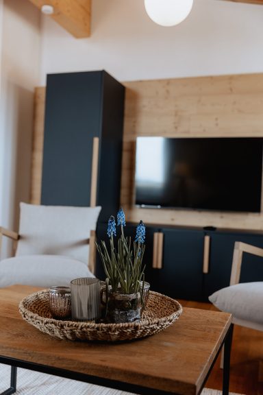 Moderne Wohnzimmereinrichtung mit Fernseher, Holzmöbeln und einer Pflanze auf einem Tisch.