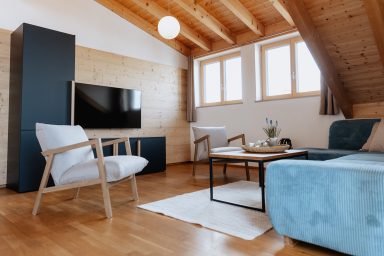 Modernes Wohnzimmer mit Fenster, TV, Stühlen und einem blauen Sofa. Holzboden und -decke.