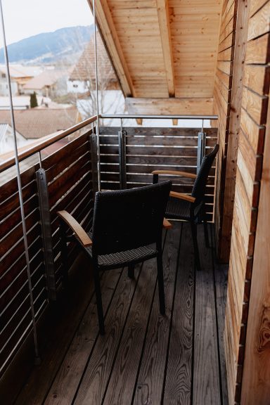 Zwei Stühle auf einem Holz-Balkon mit Dachüberstand und Blick auf die Landschaft.